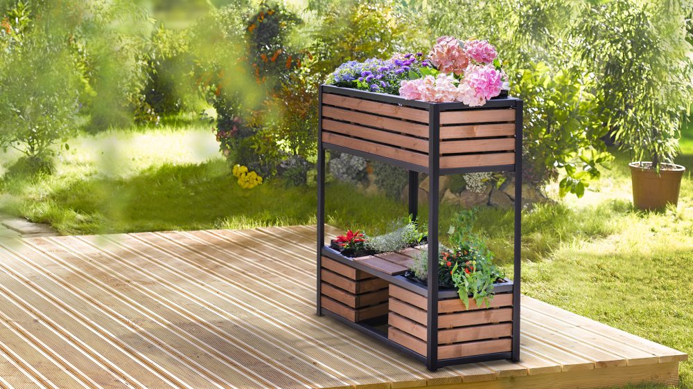 Das Hochbeet 'cube elements' klein steht, bepflanzt mit Blumen und Kräutern, auf einer Holzterrasse im Garten.